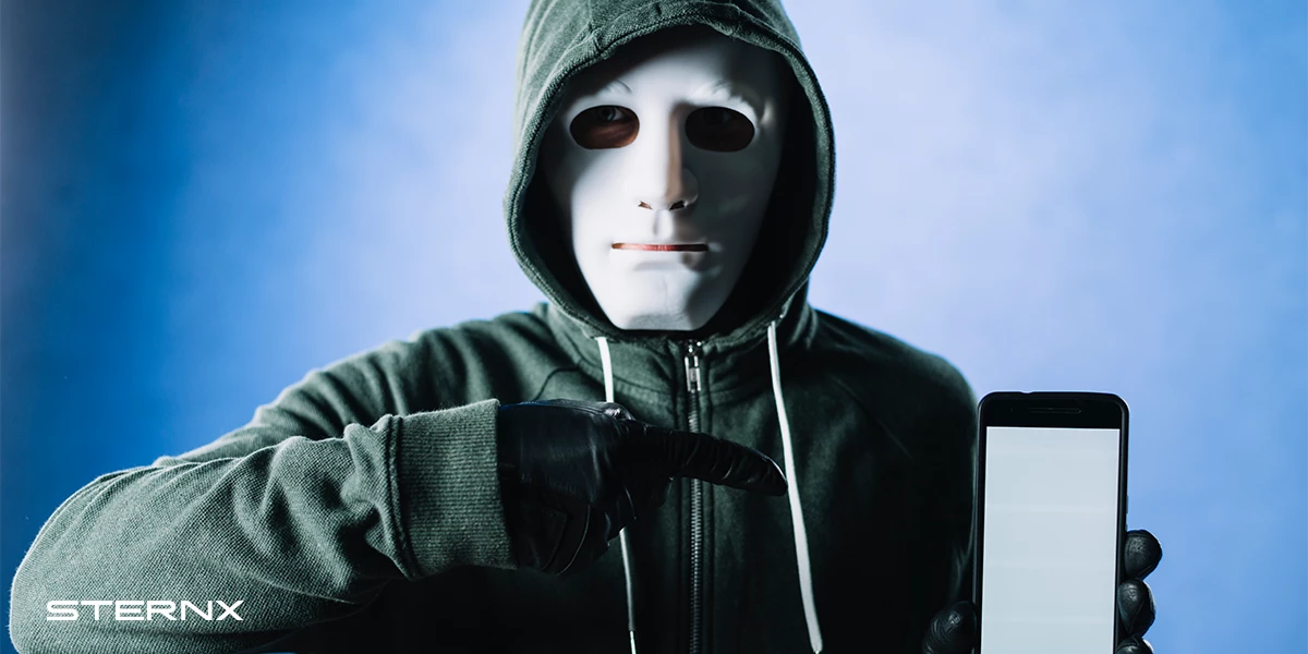 Identity Theft. A masked man in a hoodie pointing towards a blank cell phone screen